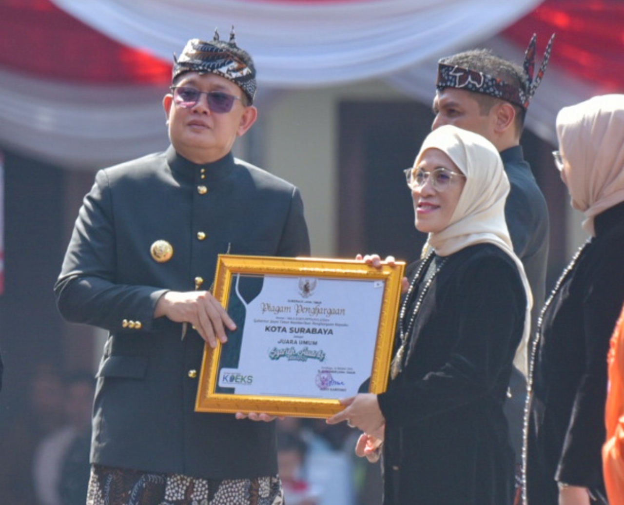 Pj Gubernur Jawa Timur Adhy Karyono menyerahkan penghargaan kepada PJs Wali Kota Surabaya Restu Novi Widiani, di Halaman Gedung Grahadi Kota Surabaya, Sabtu (12/10/2024).