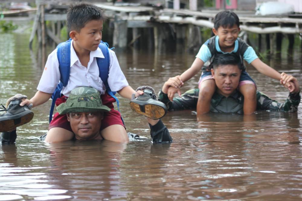 Sertu Anang Suprayitno dan Pratu Erwansyah menyunggi (menggendong dengan posisi di leher) anak menyeberangi banjir.