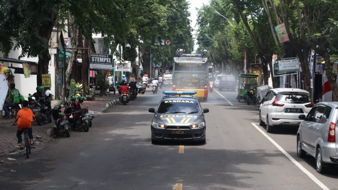 Mobil Water Canon Satuan Sabhara Polres Gresik melakukan penyemprotan disinfektan di Jalan Usman Sadar, Gresik yang padat aktivitas, Senin (8/2/2021). (TBK/BACASAJA.ID)