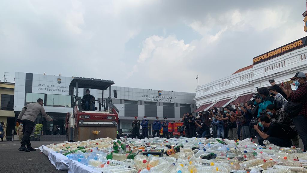 Kapolrestabes Surabaya Kombes Jhonny Eddizon Isir melempar botol miras ke arah alat berat vibro roller saat pemusnahan barang bukti 4696 botol miras di halaman Mapolrestabes Surabaya, Selasa (13/4/2021).