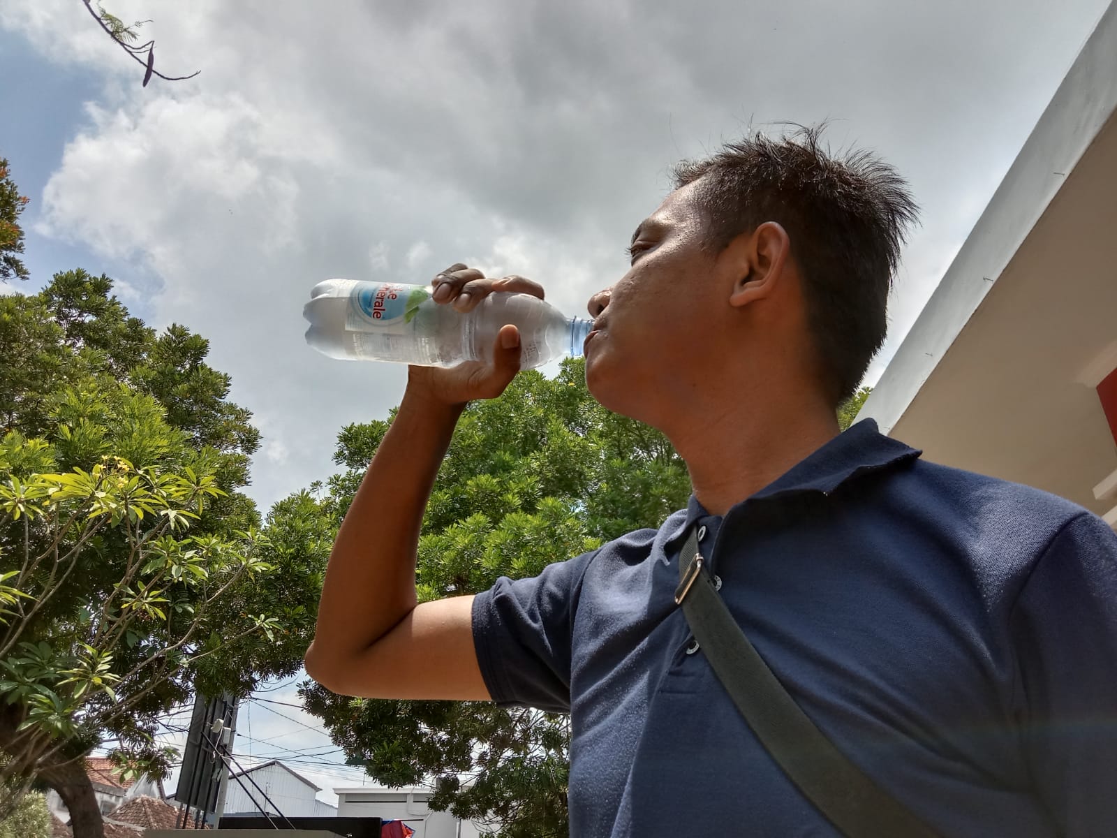 Panas, seorang pria minum air putih untuk menggantikan cairan tubuh yang hilang melalui keringat (Joko Pramono)