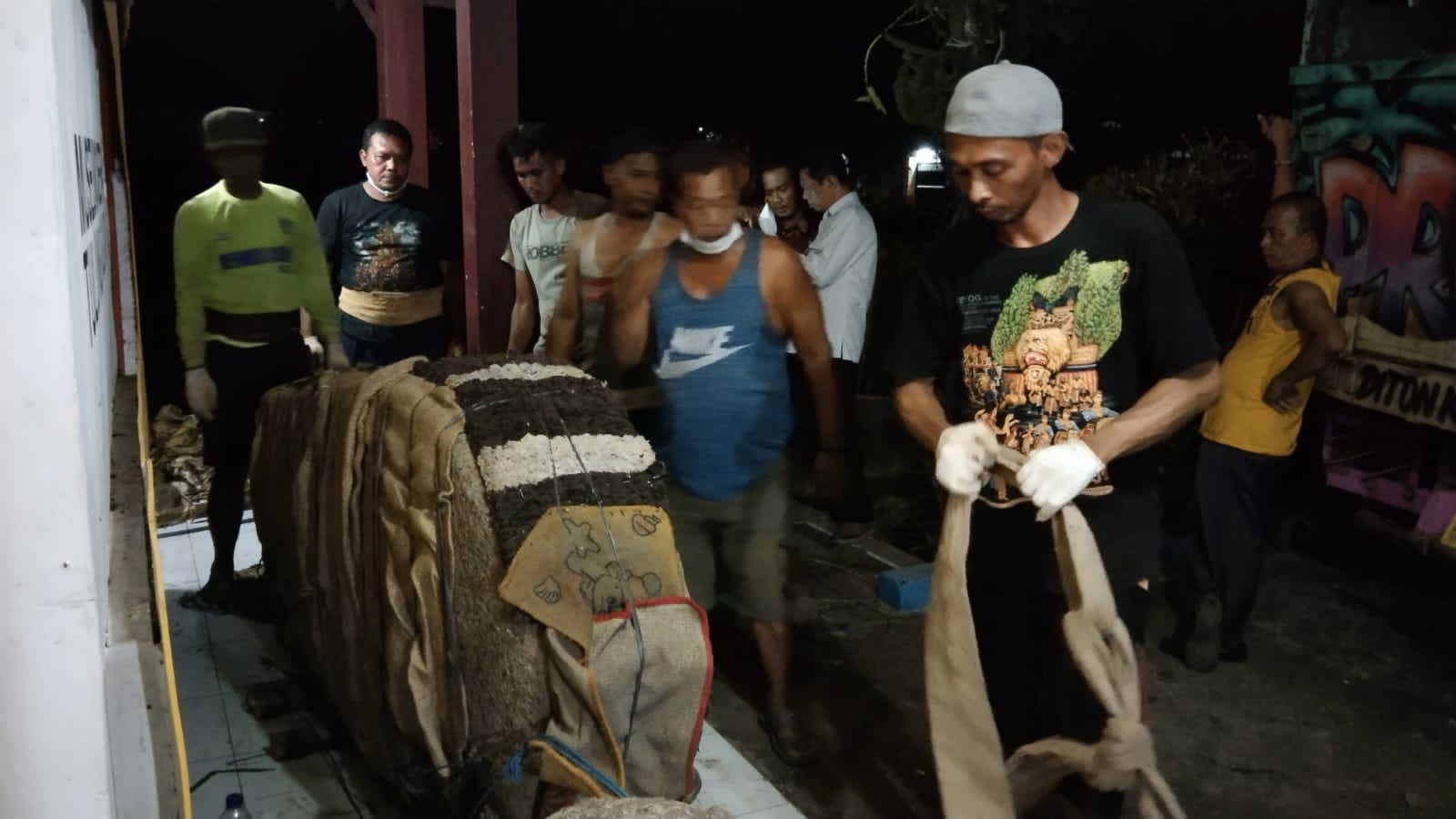 Pekerja sedang mendorong prasasti Kamulan untuk dinaikan ke atas truk.