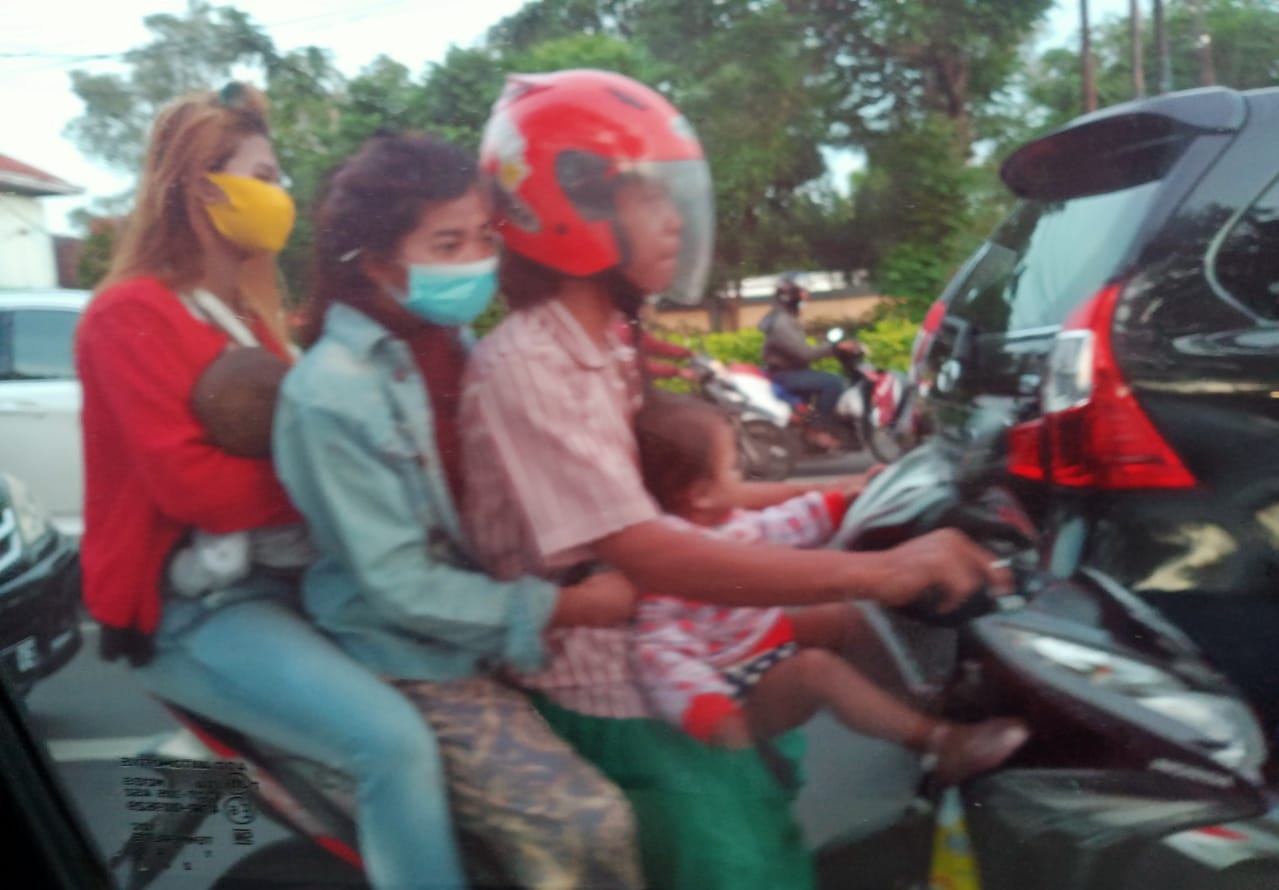 Bapak bersama 3 anak dalam satu sepeda motor berboncengan depan dan belakang melintas di jalan MERR Surabaya yang padat.