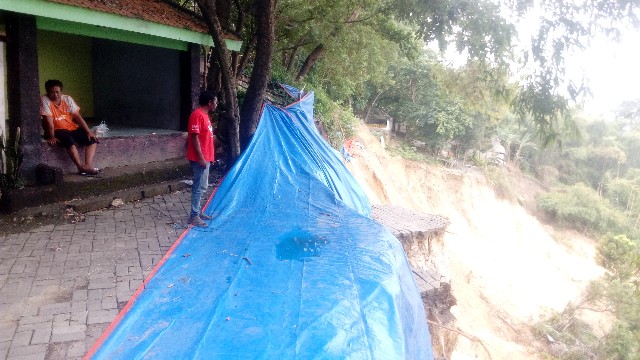 Warga sedang melihat tebing bukit Putri Cempo yang longsor di sisi sebelah timur bagian barat yang menghilangkan jalan alternatif, Kamis (4/3/2021). (TBK/Bacasaja.id)
