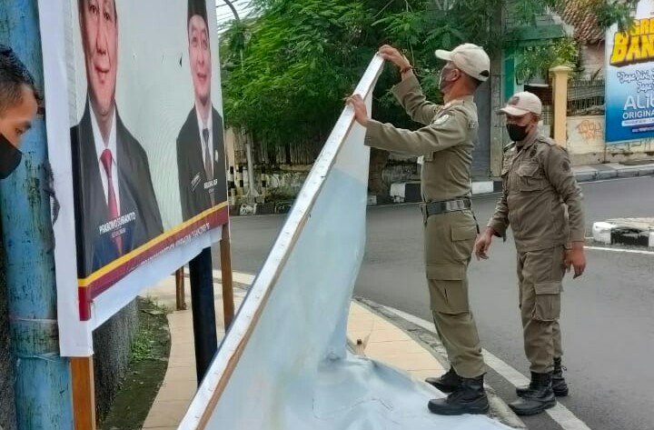 Petugas Satpol PP Gresik menurunkan reklame yang rusak yang membahayakan pengguna jalan di jalan Veteran, Jumat (19/2/2021). (TBK/Bacasaja.id)