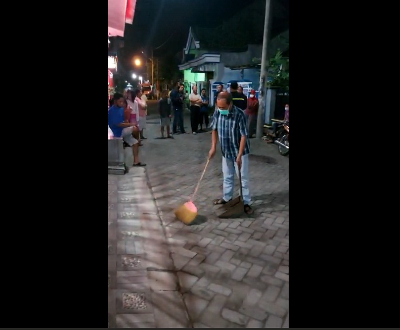 Pelaku Heru saat membersihkan halaman rumah Kacab Disdik Tulungagung-Trenggalek dari beras kuning yang disebarnya.